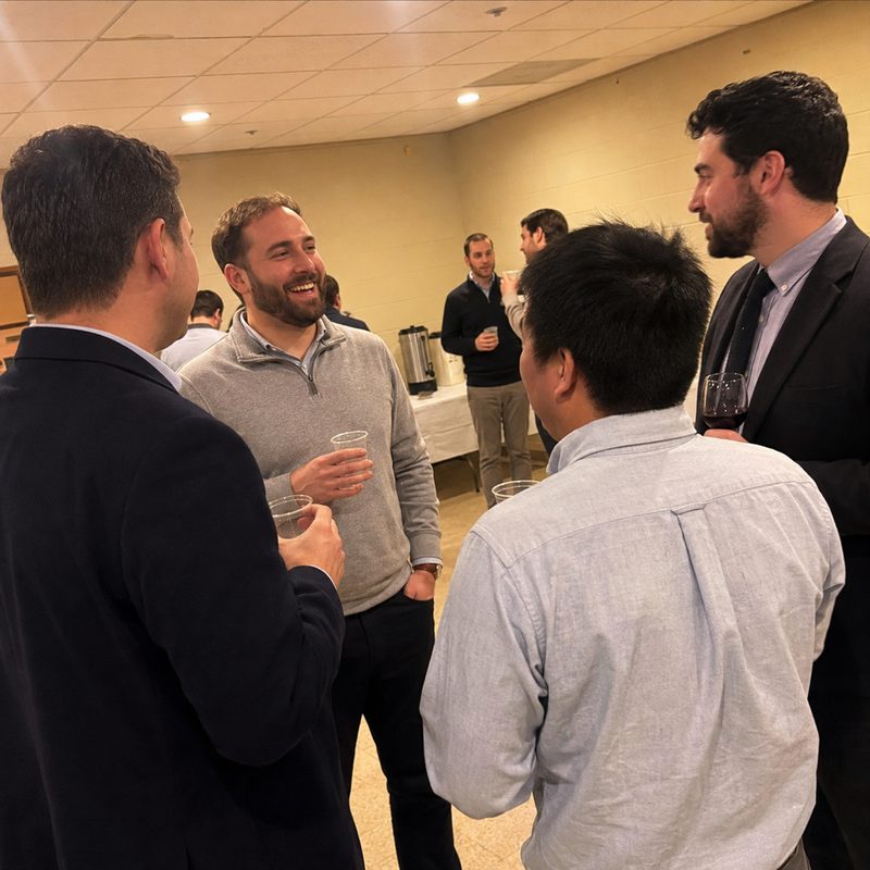 Illustration of the reception: four men standing in conversation with drinks in a parish hall before the talk.