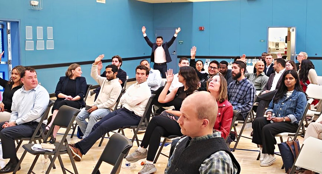 The hall during a talk seen from the side: rows of seated people, several with a hand raised.