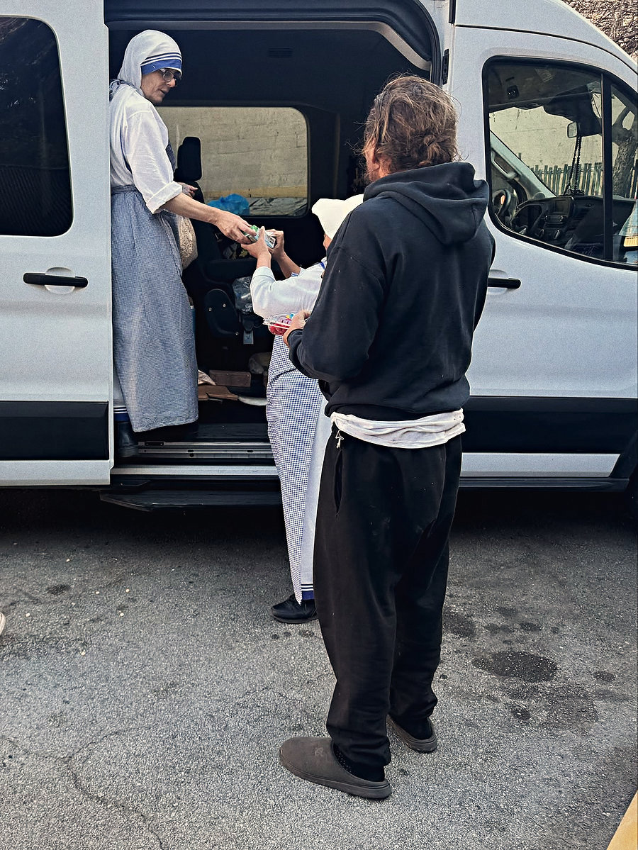 A religious sister and a volunteer handing supplies out of the back of a van on a San Francisco street during a service outing.